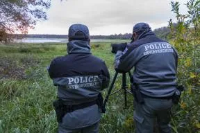 Deux agents de l'OFB en uniforme surveillent un espace naturel en regardant à travers une longue vue.