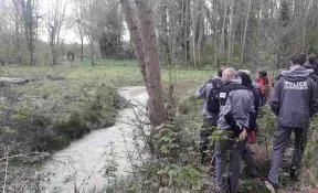 Photo de la Bièvre qui méandre au milieu des arbres. A droite, une dizaine d'agents de l'OFB en tenue de terrain observent ce cours d'eau.