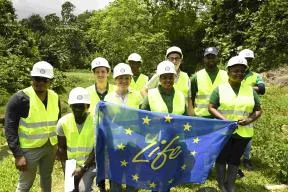 Dix personnes tiennent le drapeau "Life" de l'Europe. En fonds de la photo, un paysage mahorais.