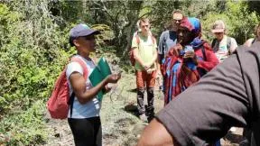 Une dame présente à plusieurs personnes au milieu de la nature une plante 