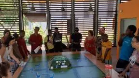 Plusieurs personnes sont autour d'un très grand table. Ils écoutent tous les régles du jeu sérieux qui est devant eux.