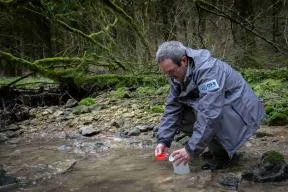Photo d'un agent de l'OFB réalisant un prélèvement d'eau dans une rivière