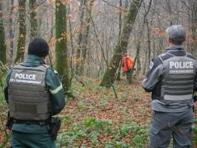 Un agent de l'OFB et un de l'ONF, vus de dos, observent un chasseur au loin.