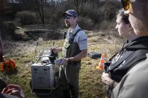 Photo : un agent de l'OFB présente le groupe électrique dédié aux pêches à l'électricité à des étudiants