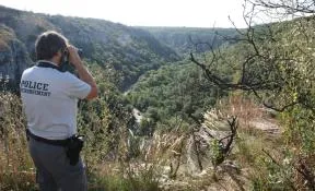 Photo représentant un agent de l'OFB vu de dos, utilisant des jumelles pour observer un espace naturel depuis un promontoire