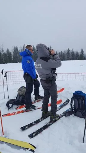 En montagne et dans un paysage enneigé, un agent de l'OFB et un gendarme surveillent la circulation des véhicules terrestes à moteur. L'agent OFB observe le paysage aux jumelles.