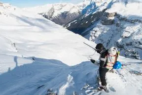 Photo d'un agent de terrain en tenue, dans un paysage enneigé, tenant une antenne rateau à la main droite et regardant un écran/boitier dans la main gauche