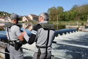 Photo de deux agents de l'OFB s'entretenant devant un cours d'eau au niveau d'un barrage.