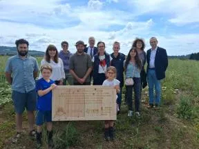 Photo d'un groupe de visiteurs du site d'IMASONIC. 2 enfants porte une plaque en bois présentant l'aménagement de la haie réservoir de biodiversité