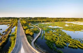 Photo vue du ciel d'une route et d'un chemin piéton et cyclable traversant une zone humide composée d'eau et de zones herbeuses