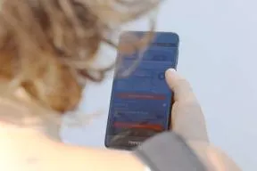 Photo d'illustration : personne de dos dont est visible l'arriere de sa tete aux cheveux blonds et le bras droit tenant un téléphone à hauteur des yeux.